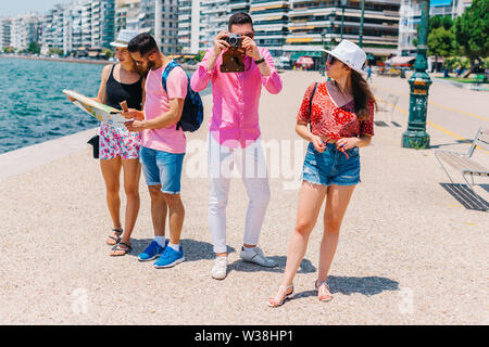 One couple is reading a map while the other is taking photos on their summer vacation. Stock Photo