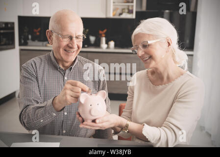 Senior couple puts the coin into the piggybank. Retirement savings concept. Stock Photo