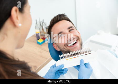 Handsome young man in stomatology clinic with female dentist. Healthy teeth whitening. Stock Photo