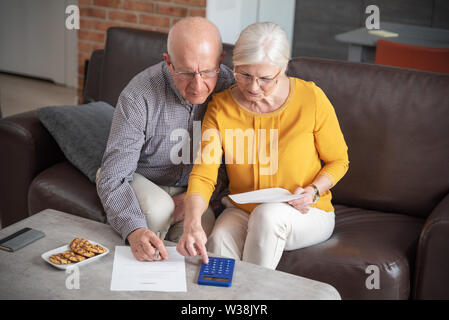 Senior couple paying bills together with calculator. Couple doing some paperwork and calculations at home Stock Photo