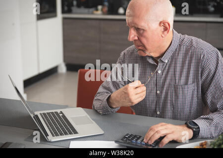 Senior man doing some paperwork and calculations at home. Pensioner counts money, tax calculation concept Stock Photo