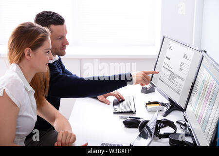 Businessman Sitting Near Businesswoman Pointing At Computer Screen Analyzing Invoice Stock Photo