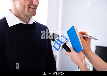 Female Journalist Writing On Diary While Taking An Interview Of Businessman Stock Photo