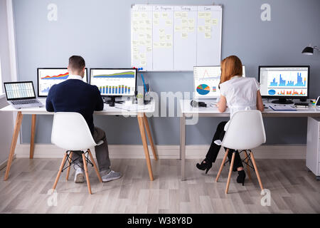Rear View Of Businessman And Businesswoman Sitting On Chair Using Computer At Workplace Stock Photo