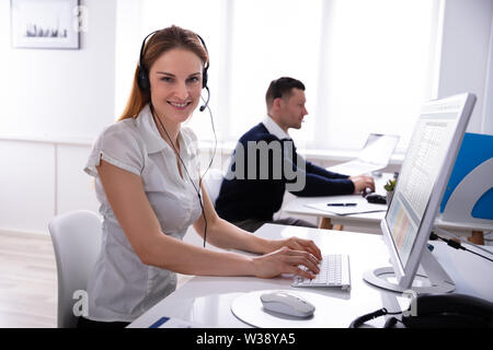 Portrait Of Young Businesswoman Sitting On Chair Wearing Headset Using Computer At Office Stock Photo