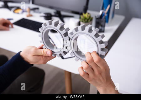 Close-up Of Two Businesspeople's Hand Connecting Gray Gears In Office Stock Photo