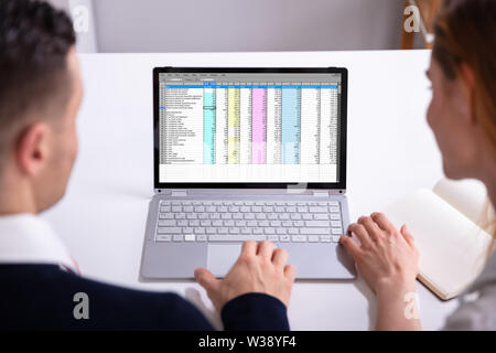 Male And Female Businesspeople Checking Spreadsheet On Laptop Screen Over Desk Stock Photo