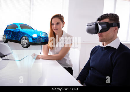 Man Wearing VR Headset Looking At Car Model Sitting Near Female Agent Stock Photo