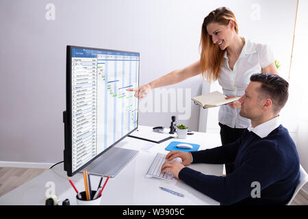 Smiling Businesswoman Pointing At Computer Screen While Businessman Analyzing Gantt Chart At Workplace Stock Photo