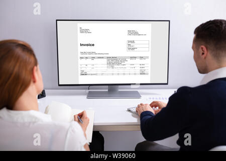 Close-up Of Two Businesspeople Analyzing Invoice On Computer Stock Photo