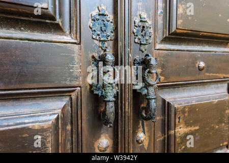 Seahorse shaped door handles on old brown wooden door in Lisbon, Portugal Stock Photo