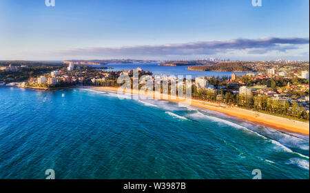 Clean straight stripe of sandy Manly beach on Sydney Pacific coast facing  open wild waves in aerial view overlooking distant Harbour and city CBD. Stock Photo
