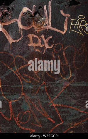 Close-up of colorful graffiti tags and spray paint on a dark, rusty metal surface with signs of weather damage Stock Photo