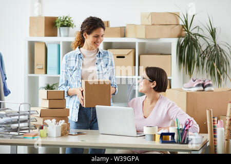 Two young managers of online shop office interacting by desk while preparing orders for clients Stock Photo