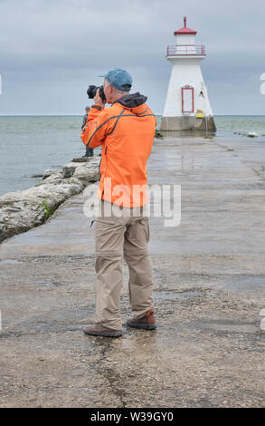 Photographer wearing bright orange jacket takes pictures on a cool dreary and rainy morning near a lighthouse. Stock Photo