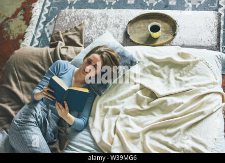 Young woman reading book on bed in the loft room, slow life Stock Photo