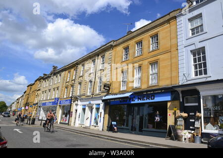 People cycling past the shops in Chipping Norton, Oxfordshire, UK. Part of the Cotswolds Stock Photo