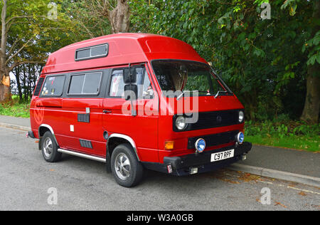 Red Volkswagen Camper Van Parked in front of trees. Stock Photo