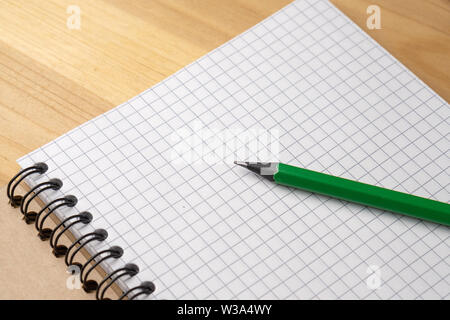 Green pencil on a notebook with sheets in a cage on a wooden table Stock Photo