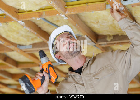 male builder using drill on wooden ceiling framework Stock Photo