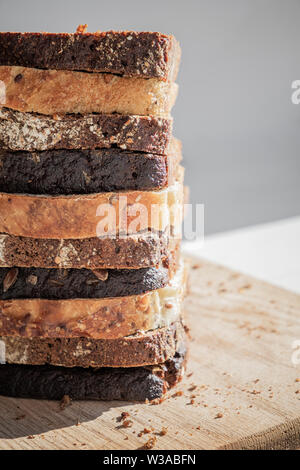 Heap of wholemeal bread slices on a cutting board. Diverse types of whole grain bread in natural light. Stock Photo