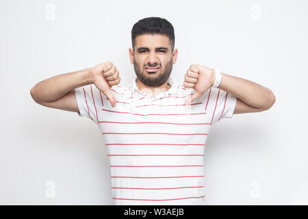 I don't like this. Portrait of displeased bearded young man in striped t-shirt standing with thumbs down dislike sign gesture and looking at camera. i Stock Photo