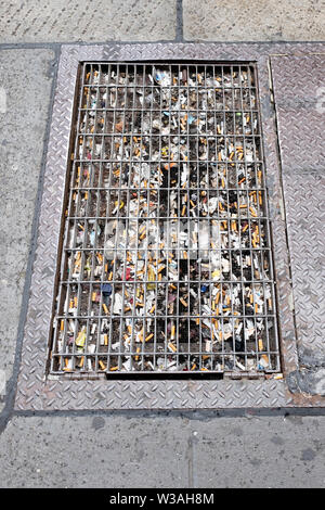 Multiple cigarette butts in a grating outside a small office building in the spot where workers take their smoking break. On Broadway in Manhattan, NY Stock Photo