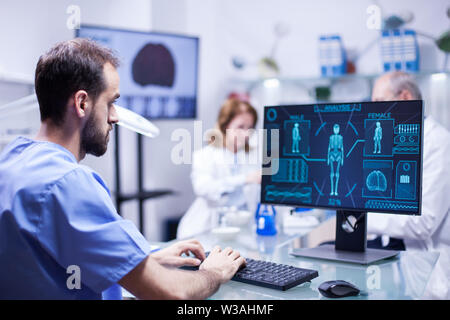 Young technician typing data for human body neurology system in science laboratory. Specialist working. Stock Photo