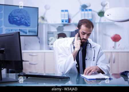 Male doctor talking on the with one of his patients from his hospital cabinet. Handsome doctor in uniform. Stock Photo