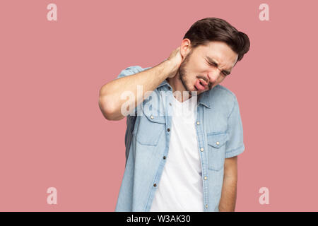 Neck or back pain. Portrait of sad sick handsome bearded young man in blue casual style shirt standing and holding his painful neck and feeling bad. i Stock Photo