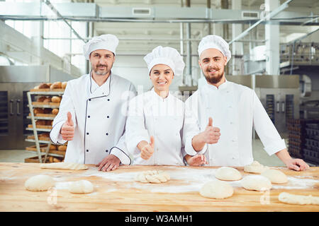 Bakers raised their thumbs up on the background of the bakery. Stock Photo