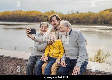 Senior couple with with grandson and great-grandson take a selfie in the autumn park. Great-grandmother, great-grandfather and great-grandson Stock Photo