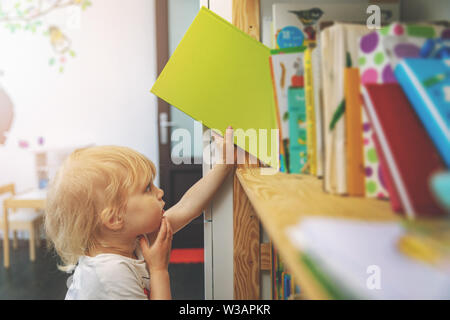 little girl choosing and taking book from shelf to read Stock Photo