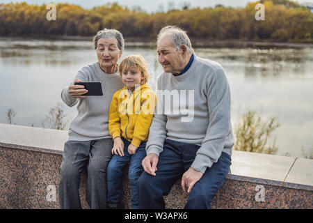 Senior couple with great-grandson take a selfie in the autumn park. Great-grandmother, great-grandfather and great-grandson Stock Photo