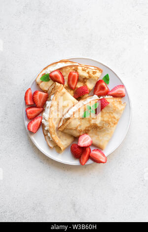 Crepes with ricotta cheese and fresh strawberries on white background, top view, copy space. Delicious crepes, thin pancakes. Stock Photo