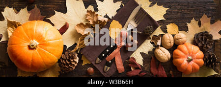 Thanksgiving Table Setting, top view, banner. Autumnal holiday decorated table with pumpkins, cutlery, yellow leaves. Stock Photo