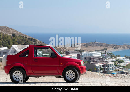 Compact red offroad vehicle on hilltop, with panorama and sea view in background. Kos island, Greece, on a hot summer day. Stock Photo