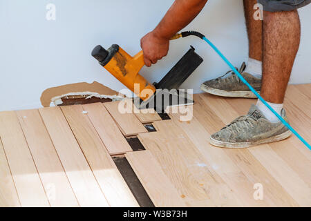 Carpenter worker installing wood parquet board during flooring work with hammer Stock Photo