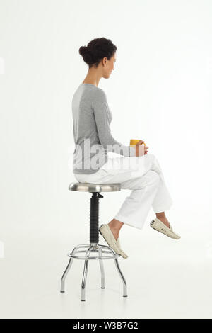 Caucasian woman sitting on a stool and having a cup of coffee Stock Photo