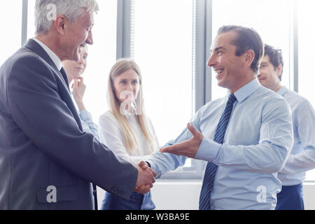 Happy business shaking hands in modern office Stock Photo
