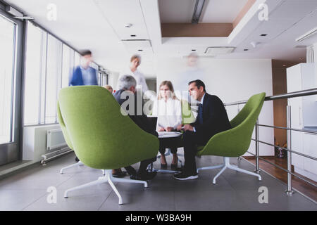 Business people sitting together on armchairs in office hall and having a discussion Stock Photo