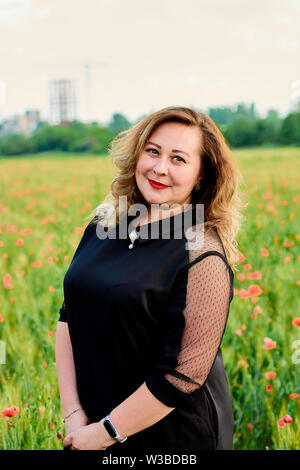 Long-haired plus sized woman in a black dress on a field of green wheat and  wild poppies. Overweight fat woman. The concept of freedom and freshness  Stock Photo - Alamy