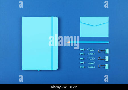 Neatly organized stationery flat lay of pastel blue notebook, envelope, pencil, office clips, binders and pins in order over dark indigo blue backgrou Stock Photo