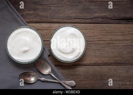 White yogurt in two glass bowls on old wooden desk with two spoons next to. Stock Photo