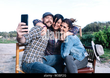 A group of friends sitting outdoors while taking a selfie with friends. They are posing and smiling. Stock Photo