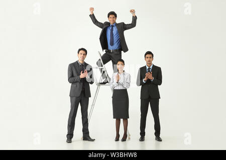 Businessman standing on ladder being applauded by colleagues Stock Photo