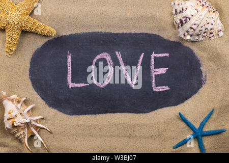Handwritten chalk inscription LOVE on blackboard, lying among the seashells and starfish on the sand. Top view Stock Photo