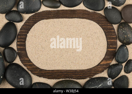 Frame of dark wood on the sand and black stones around. With space for design, text place. Top view Stock Photo