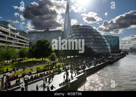 Tourists at Potters Fields Park on the shore of the River Thames with spire of The Shard and curved City Hall London England Stock Photo