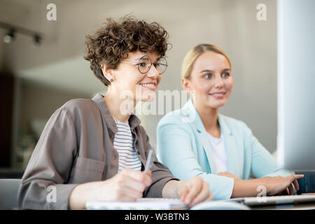 Two happy female colleagues looking at data on computer screen Stock Photo